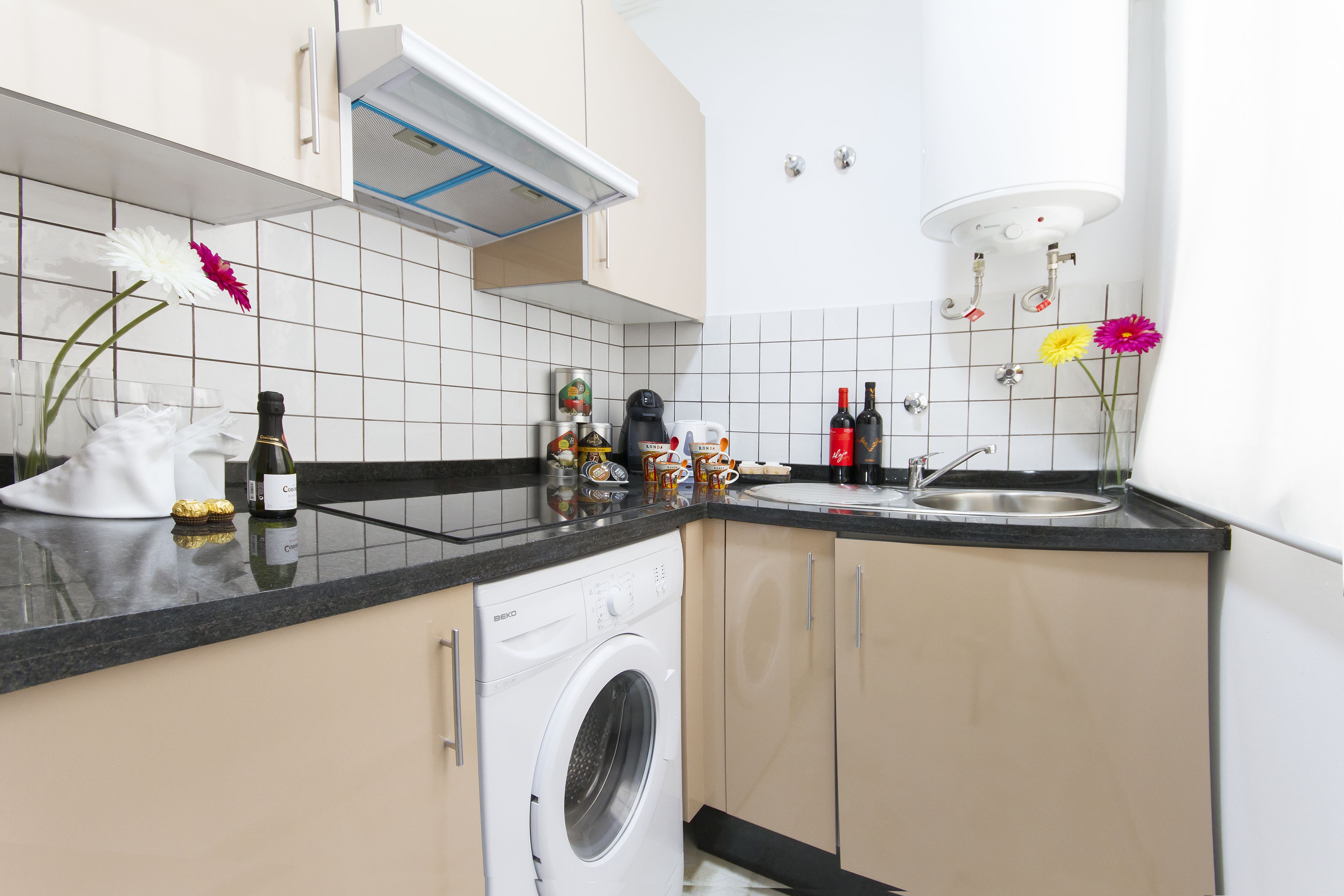 Una cocina moderna con lavadora incorporada, un fregadero y una encimera con diversos objetos.