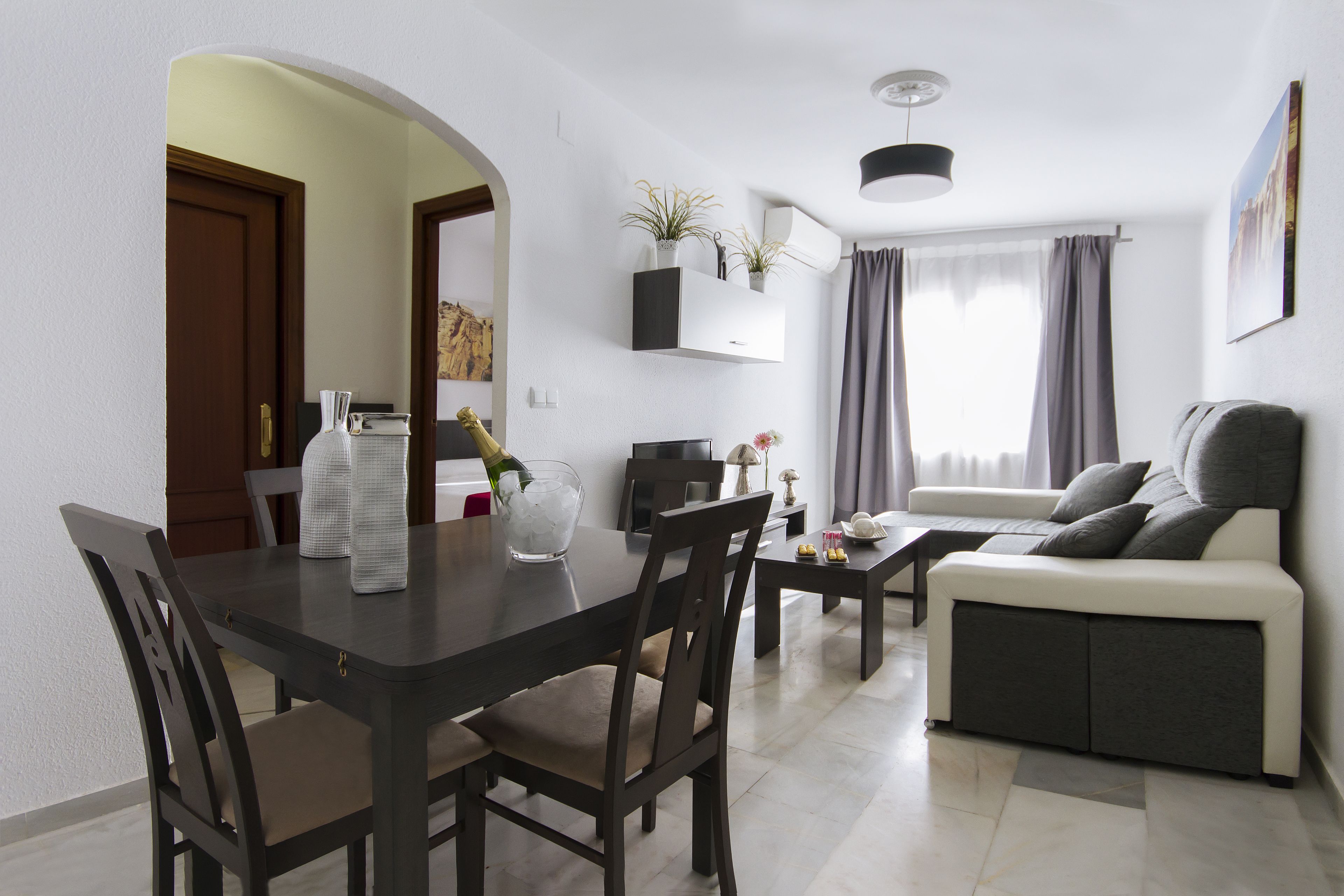 A modern living room with a sofa, a dining table with chairs, and a kitchen area in the background.