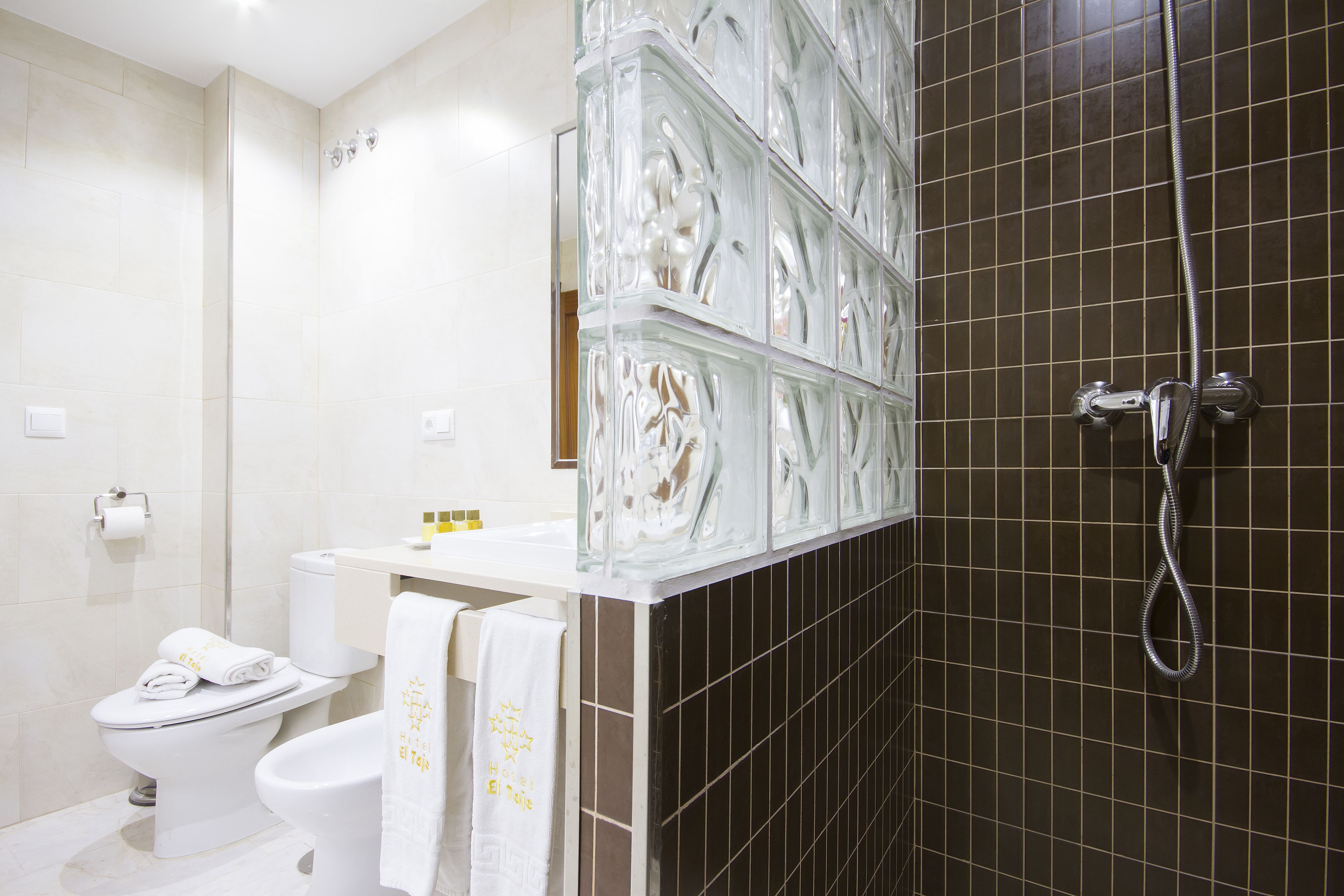Un baño con inodoro, bidé y zona de ducha con mampara de vidrio.