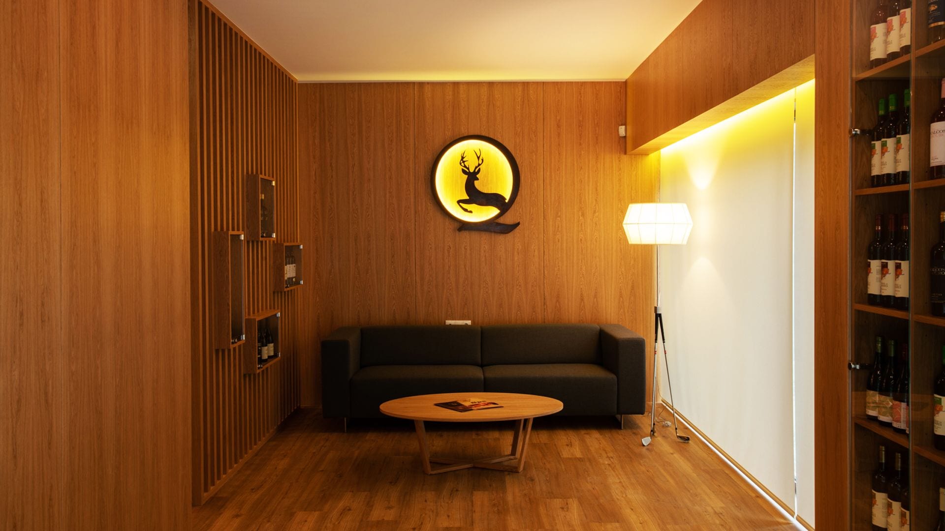 A modern room with a wooden panel wall, a round wall decoration, a dark sofa, a small wooden coffee table, and a wine rack.