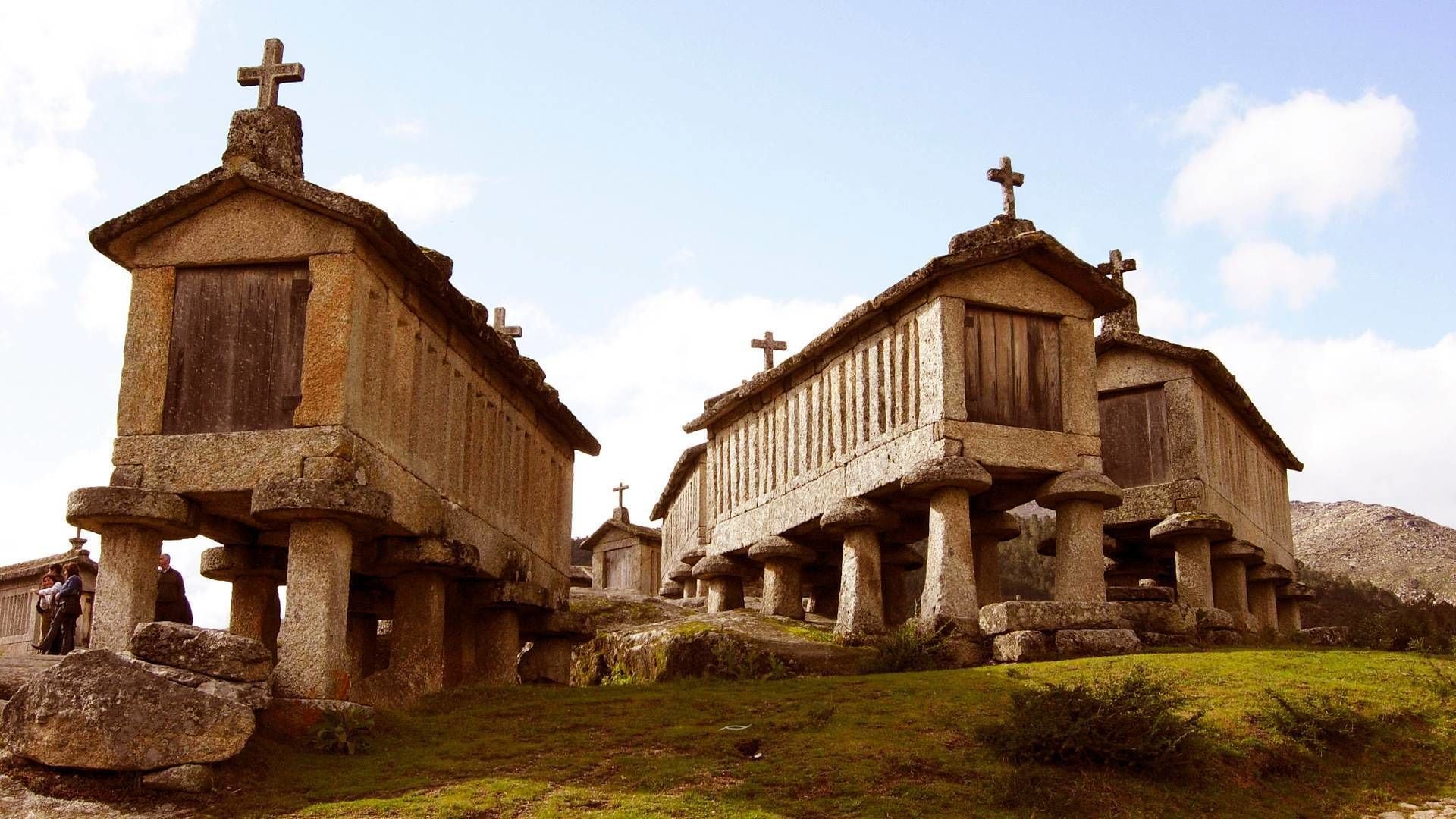 Una iglesia de piedra con varias cruces en la parte superior, rodeada de un área cubierta de césped y otras estructuras similares.
