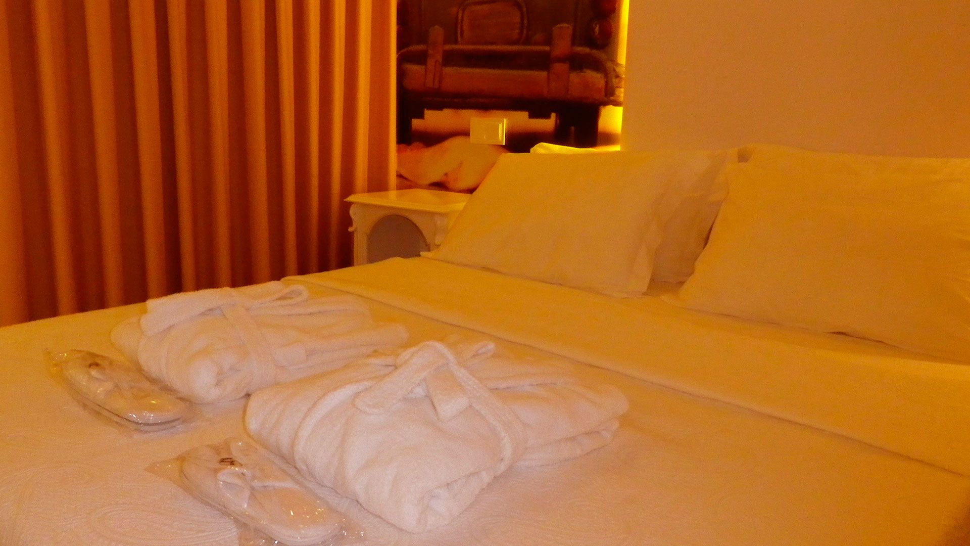 A hotel room with a neatly made bed, white linens, and two towels placed on the bed.
