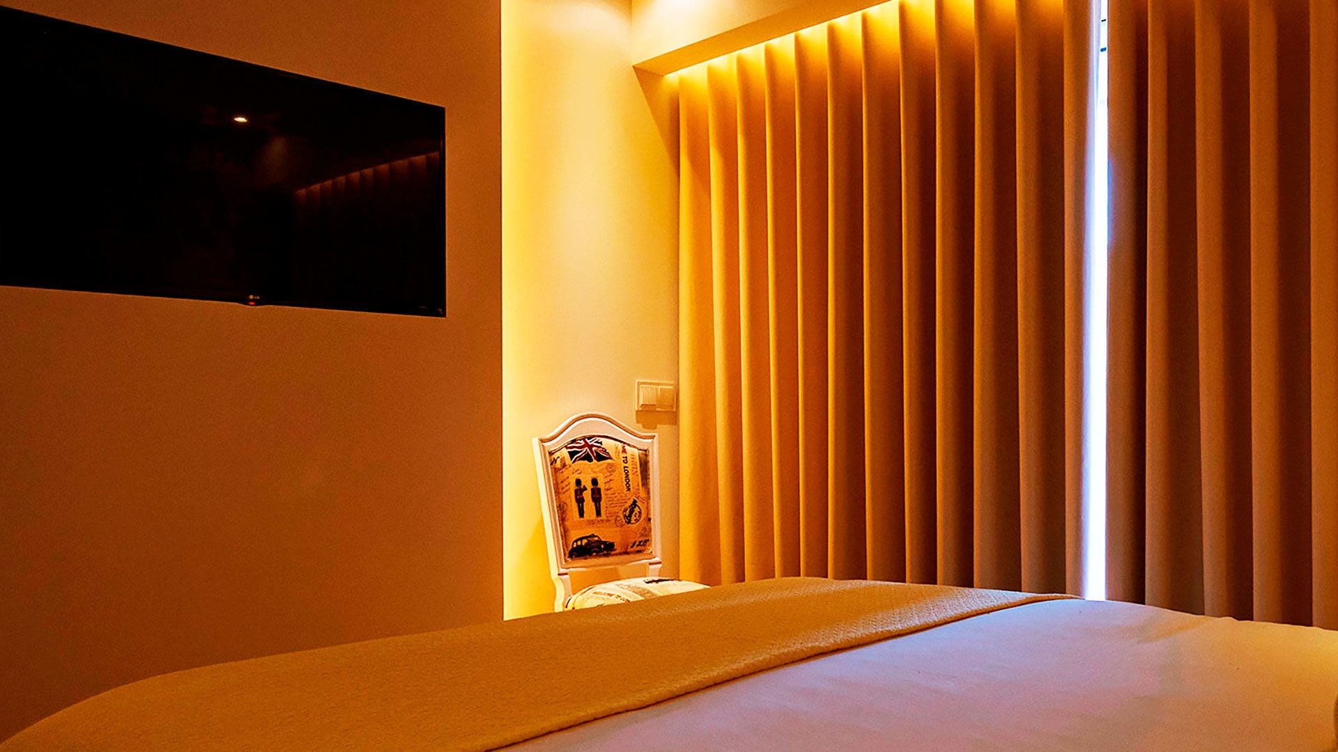 A hotel room with a bed, a television mounted on the wall, and a window with vertical blinds.