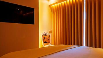 A hotel room with a bed, a television mounted on the wall, and a window with vertical blinds.