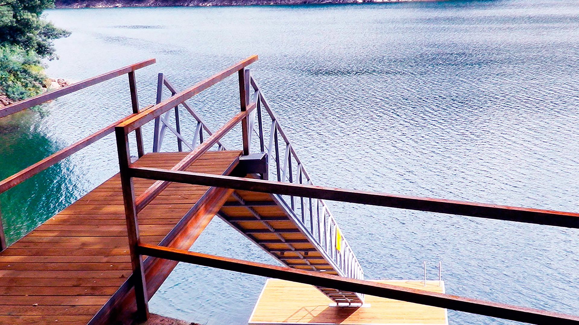 Een houten steiger die uitsteekt in een rustig meer, met een metalen hekwerk.