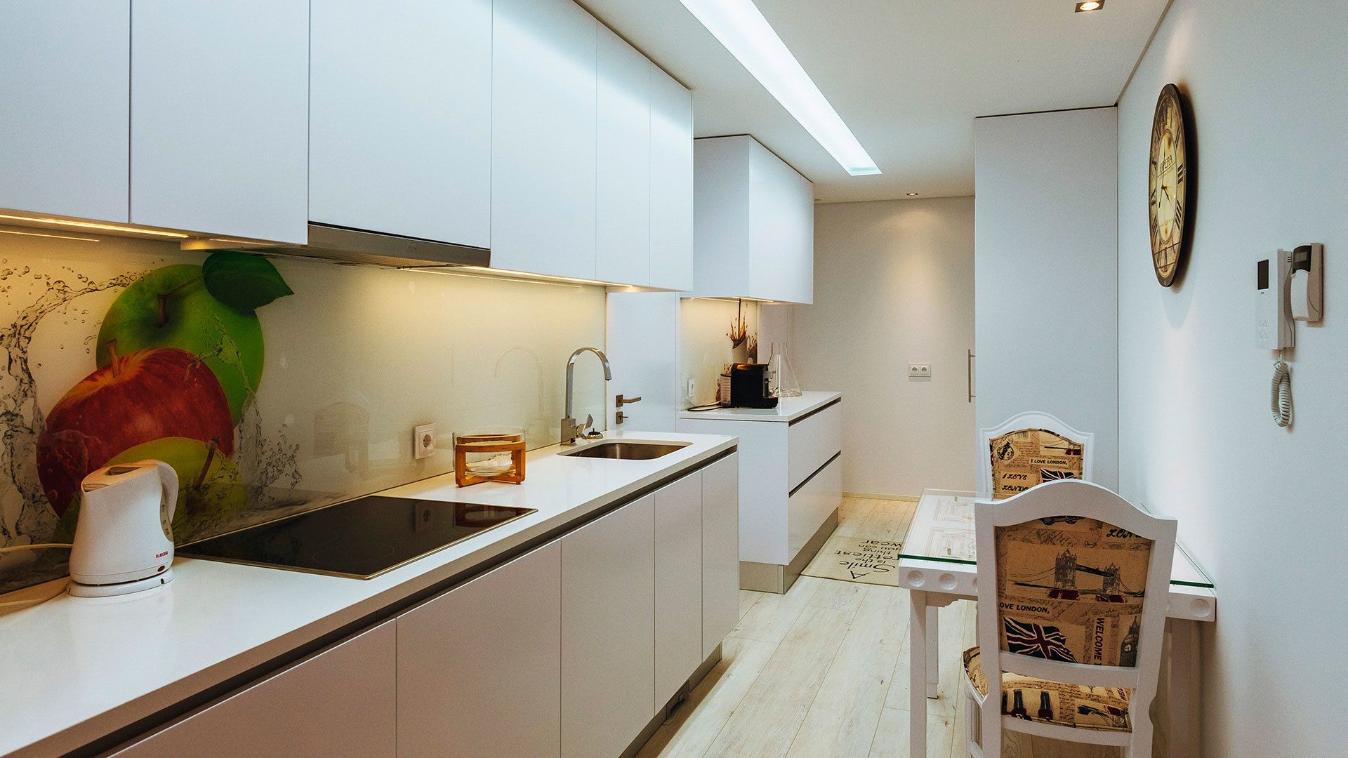 Een moderne keuken met witte kasten, een roestvrijstalen spoelbak en een eethoek met een houten stoel en tafel.