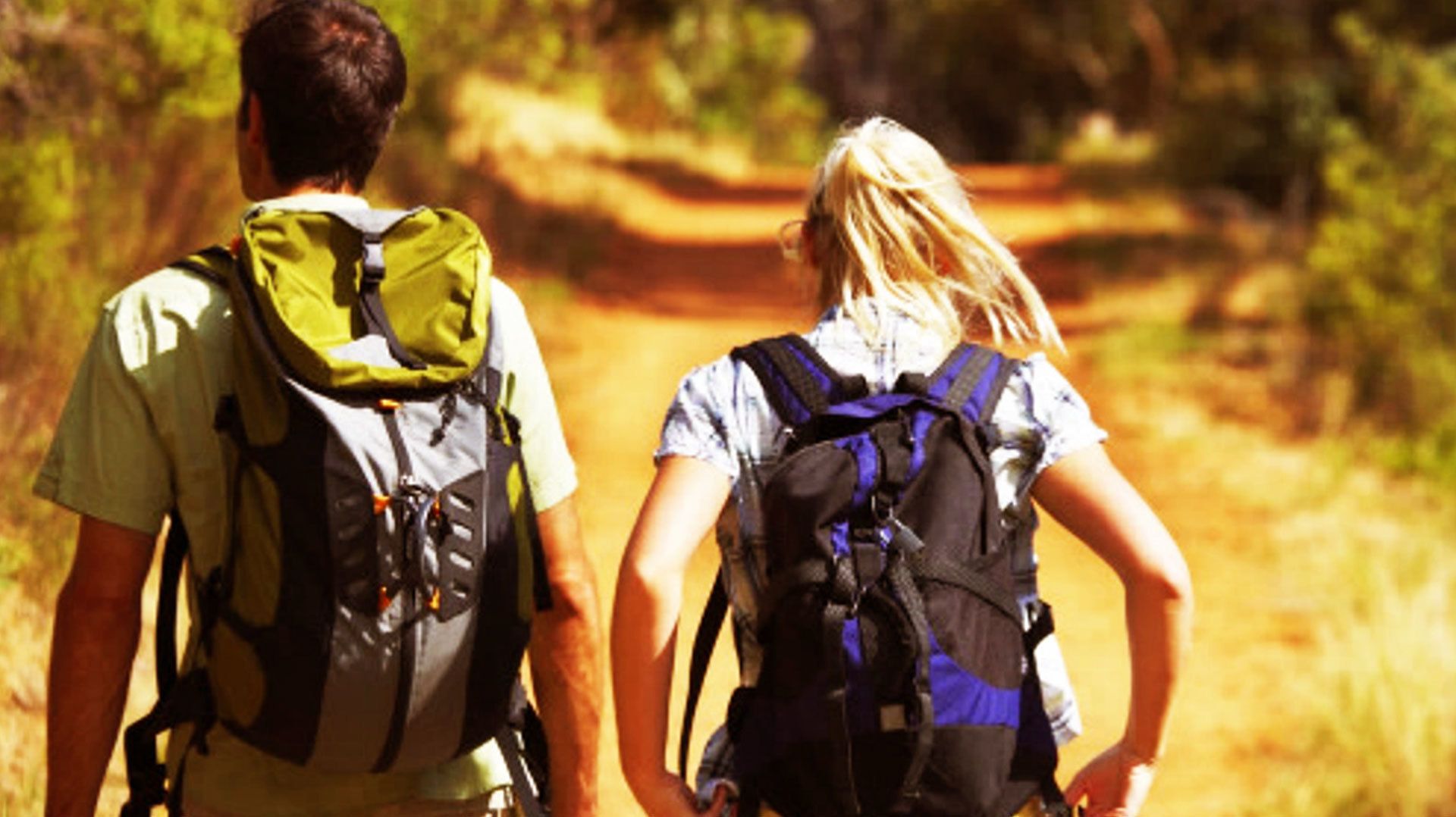 Two people walking on a dirt path with backpacks.