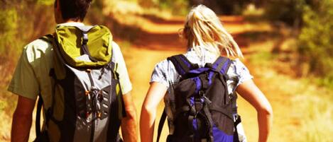 Two people walking on a dirt path with backpacks.