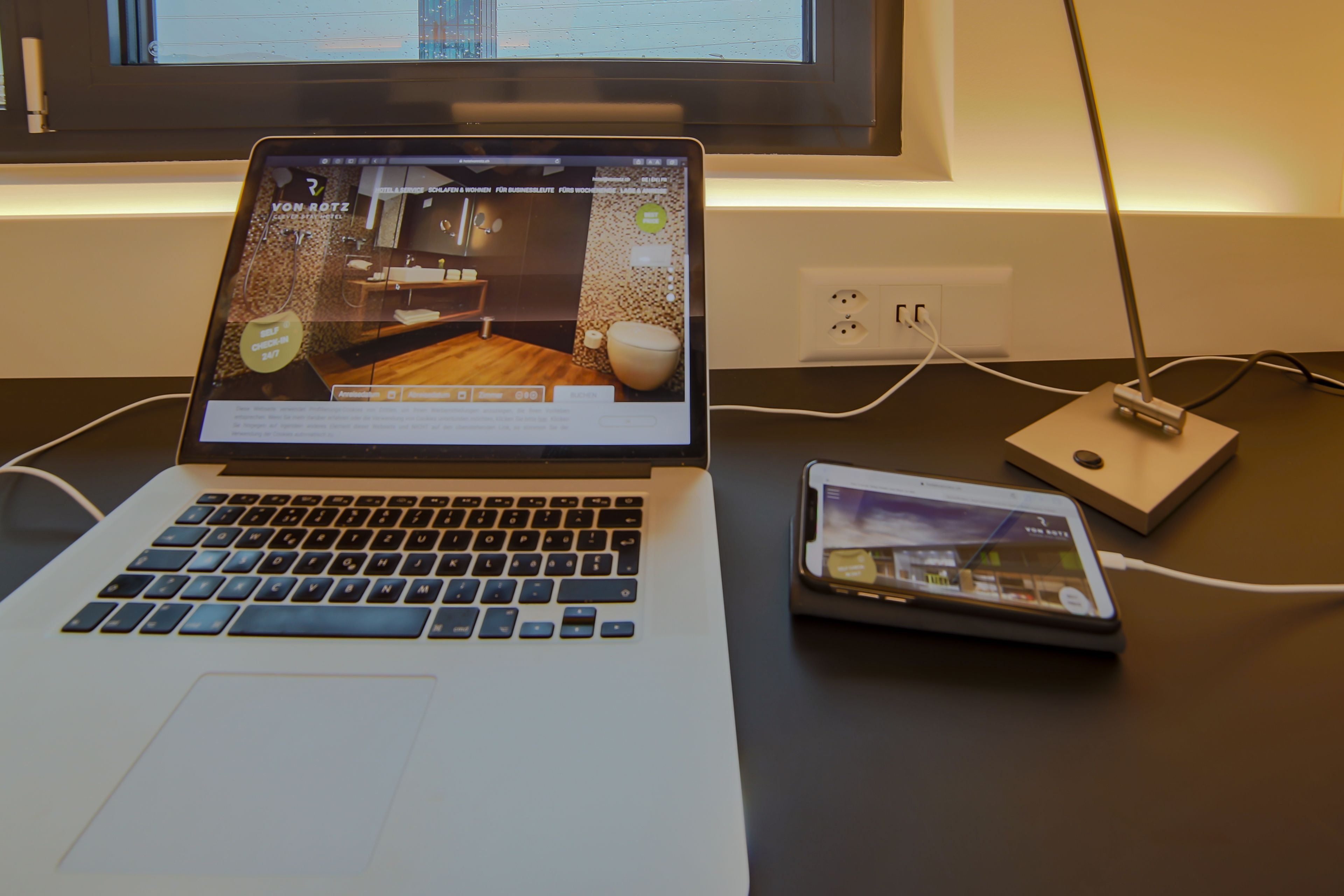 A laptop on a desk with a tablet and a power strip.