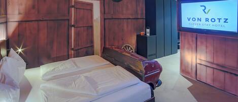 Habitación de hotel con decoración de madera, una cama, un coche antiguo y un televisor que muestra el nombre del hotel.