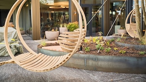 A wooden hanging chair with a cushioned seat and backrest, suspended by chains. - Hotel von Rotz (Wil)