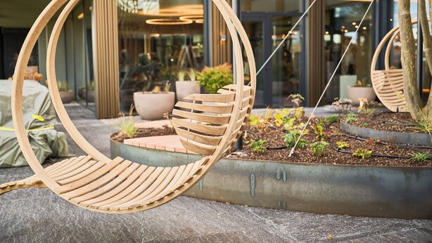 Una silla colgante de madera con asiento y respaldo acolchados, sostenida por cadenas.