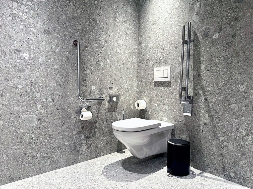 A modern bathroom with a unique, angular toilet design, a handrail, and a trash bin.