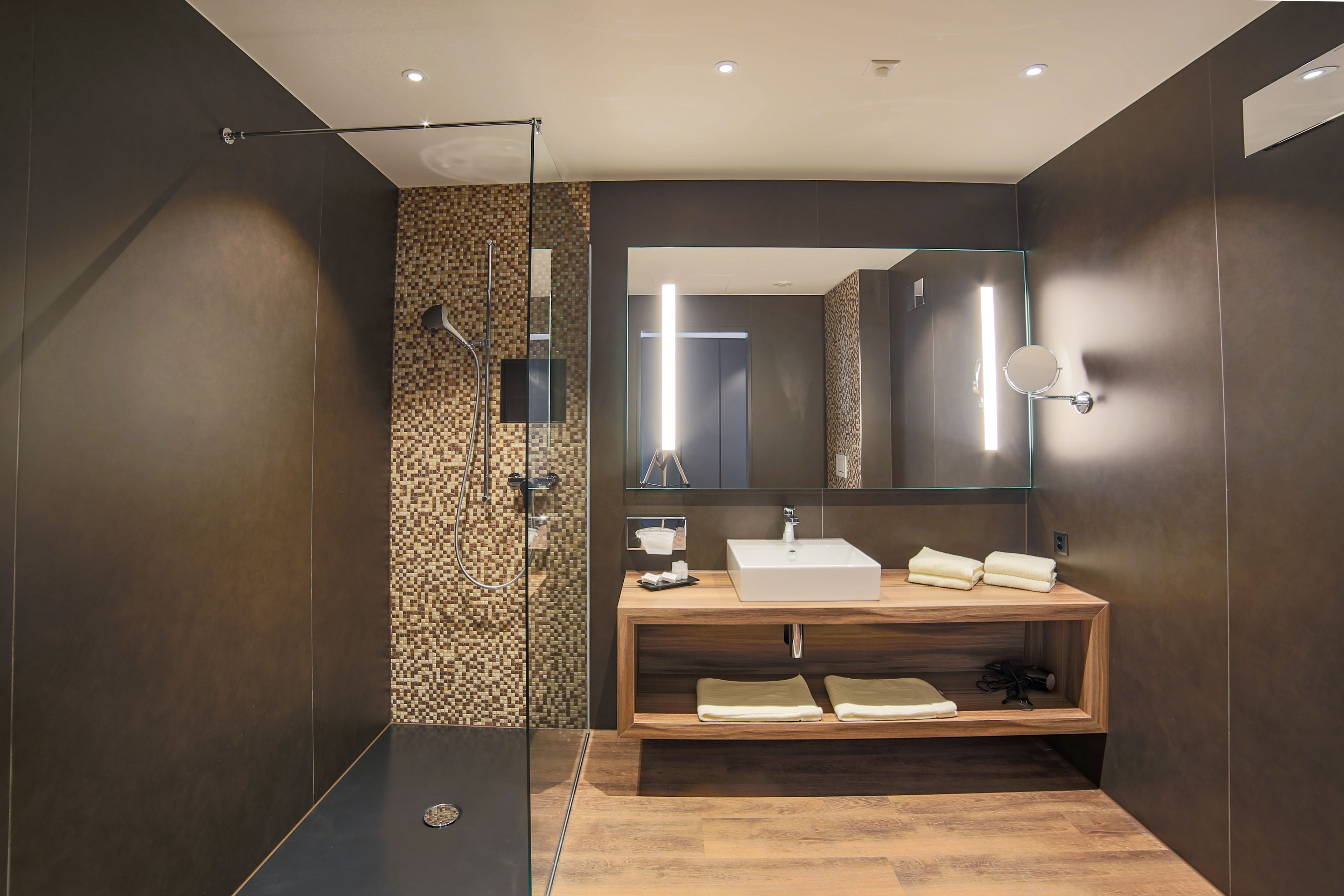 Un baño moderno con un espejo grande, tocador de madera y zona de ducha.