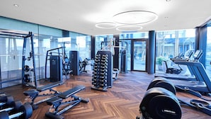Un gimnasio moderno con diverso equipamiento de ejercicio, amplias ventanas y suelo de madera.