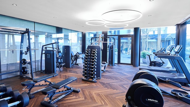 A modern gym with various exercise equipment, large windows, and a wooden floor. - Hotel von Rotz (Wil)