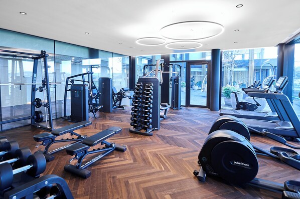 A modern gym with various exercise equipment, large windows, and a wooden floor. - Hotel von Rotz (Wil)