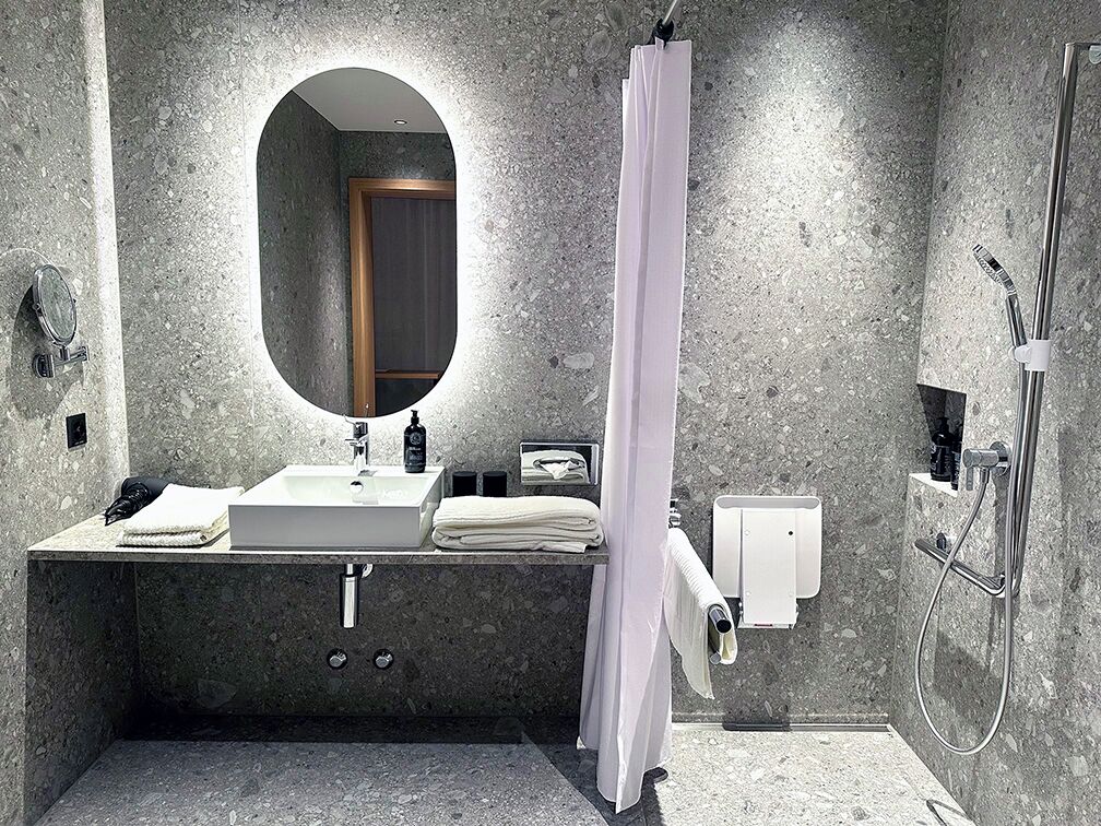 Un baño moderno con encimera de granito, un espejo redondo, ducha con cortina y cabezal de ducha manual.