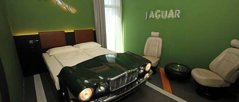 Una habitación con una cama, el emblema de Jaguar, un coche clásico, un sillón de cuero y un neumático.