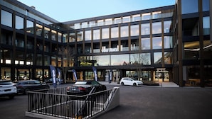 Un hotel moderno con fachada de vidrio, un restaurante y un área de estacionamiento con automóviles.