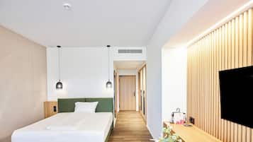 A modern hotel room with a bed, bedside table, TV, and a small kitchenette area.