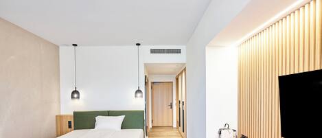 A modern hotel room with a bed, bedside table, TV, and a small kitchenette area.