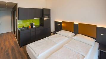Una habitación de hotel moderna con una cama, una kitchenette pequeña y una mesita de noche.