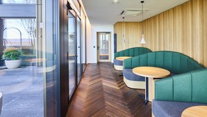 Un interior moderno con suelo de madera en patrón de espiga, asientos tapizados en verde y una puerta de vidrio que da al exterior.