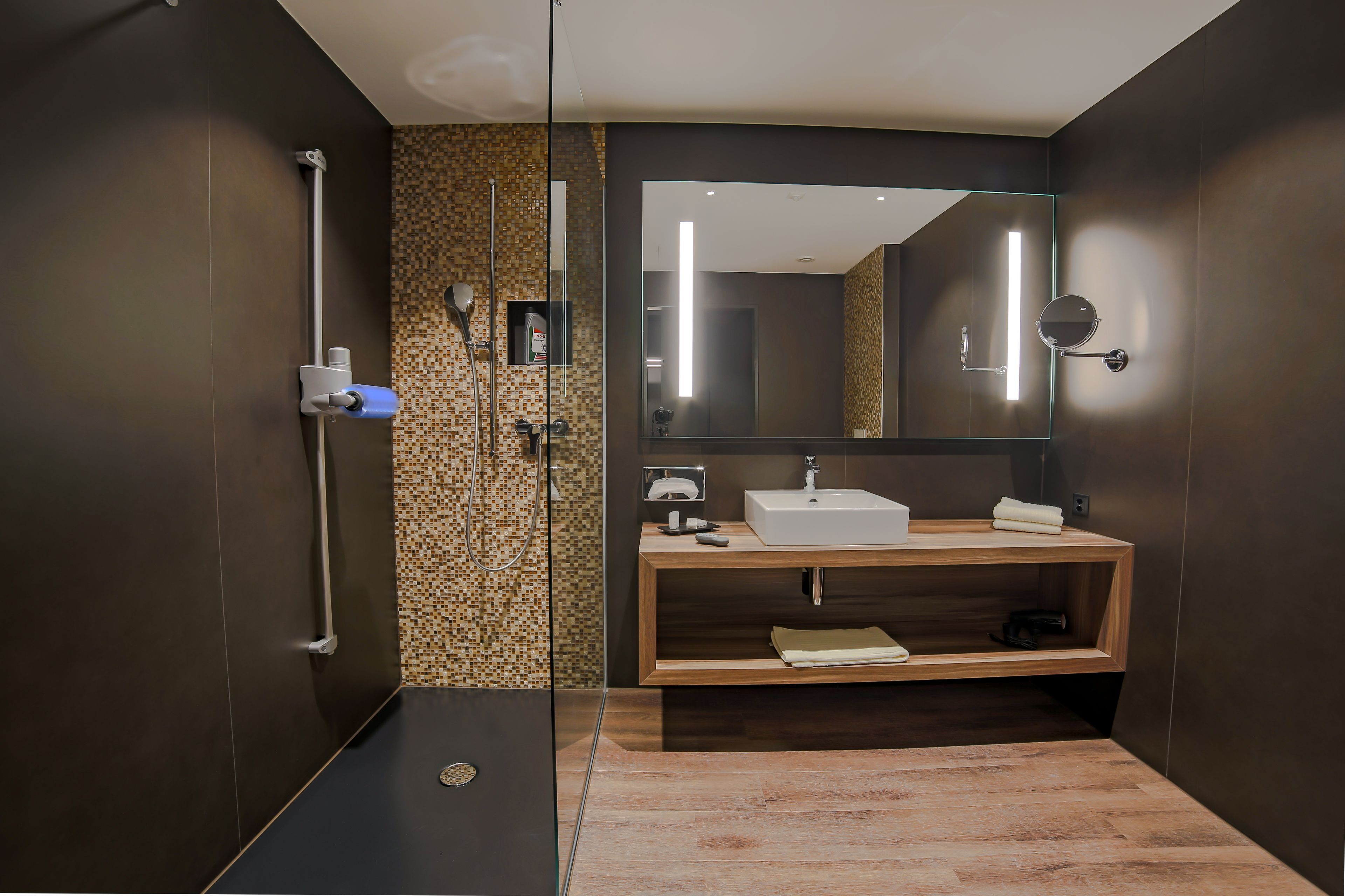 A modern bathroom with a walk-in shower, a wooden vanity, a large mirror, and a tiled backsplash.