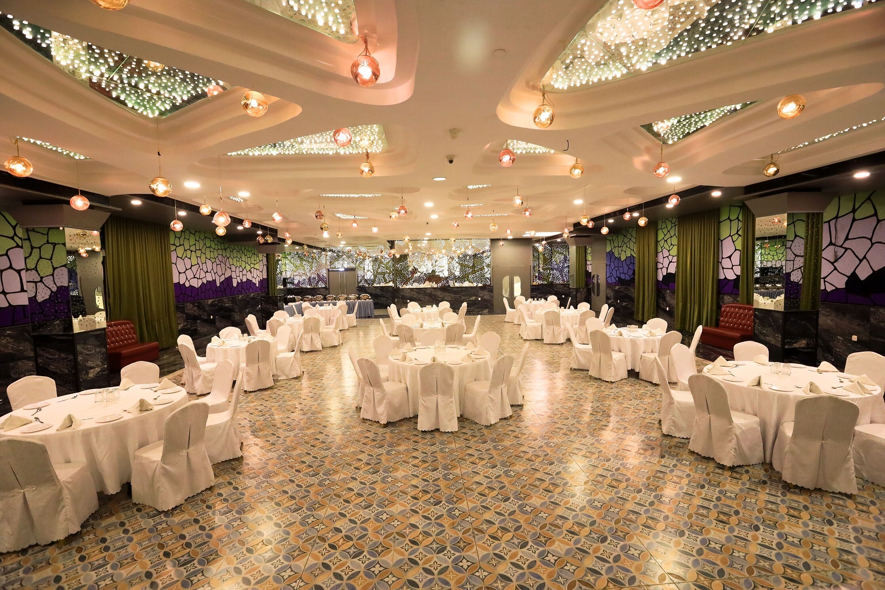 A banquet hall with round tables and white chairs, decorated with green curtains and a patterned floor.