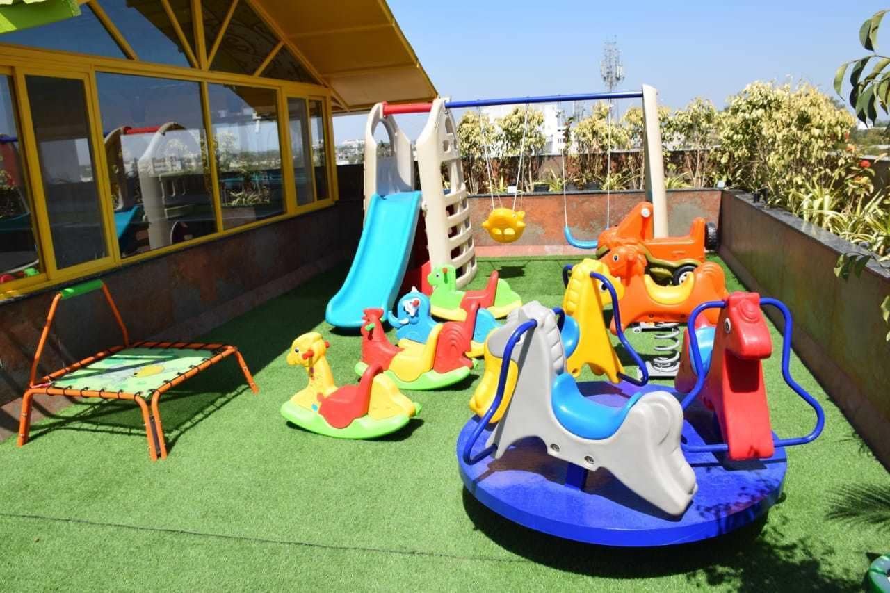 Un espace de jeux pour enfants avec un toboggan, des balançoires et un petit trampoline.