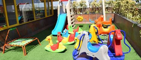 Un espace de jeux pour enfants avec un toboggan, des balançoires et un petit trampoline.