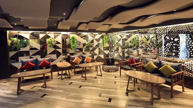 Un área de descanso moderna con paredes de diseño geométrico, muebles de madera y plantas verdes.