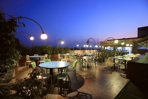 An outdoor patio area with round tables and chairs, surrounded by potted plants.