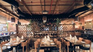 Un restaurante con mesas y sillas de madera, un separador de celosía y lámparas colgantes.
