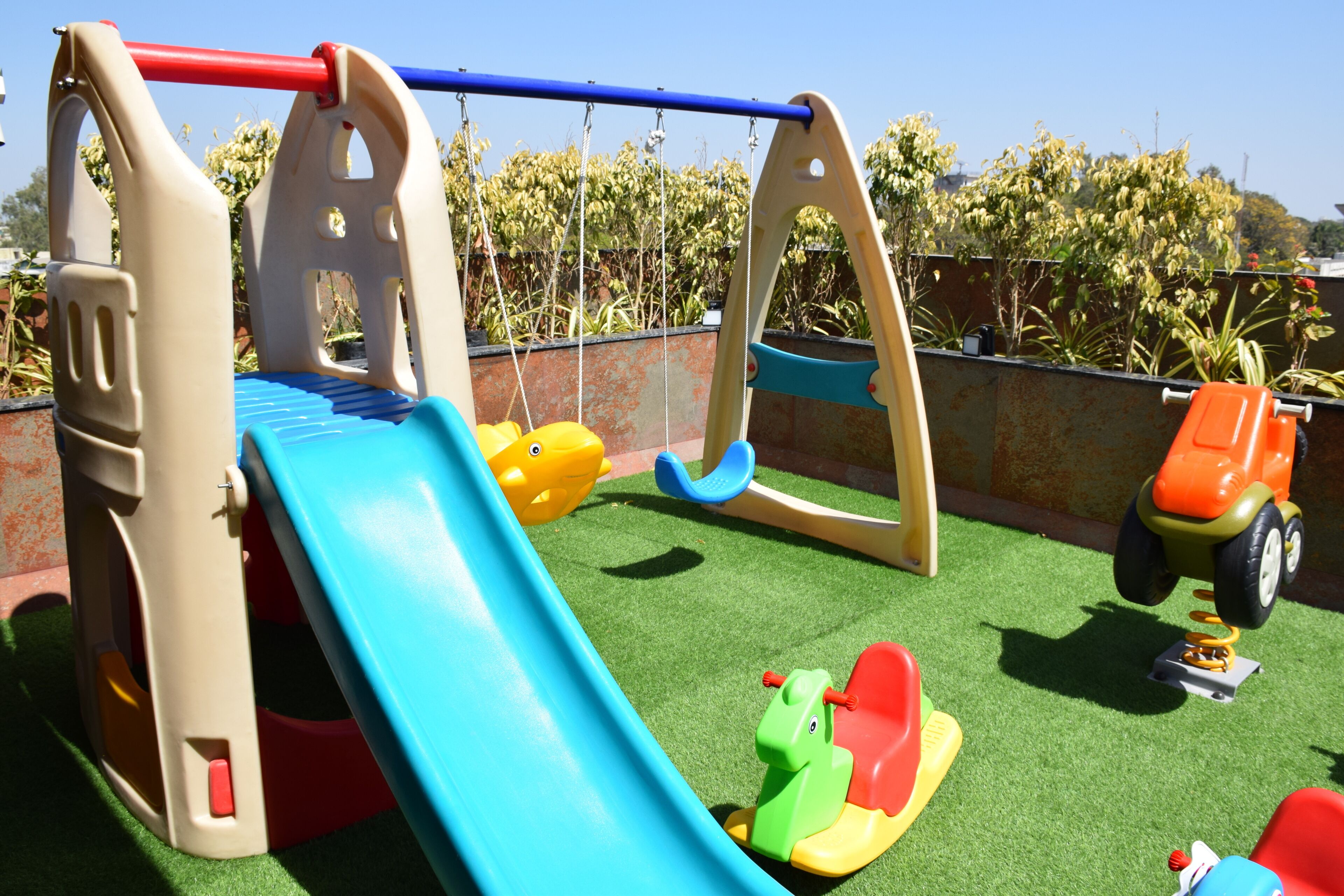 Un área de juegos infantiles con tobogán, columpios y un pequeño coche de juguete naranja.
