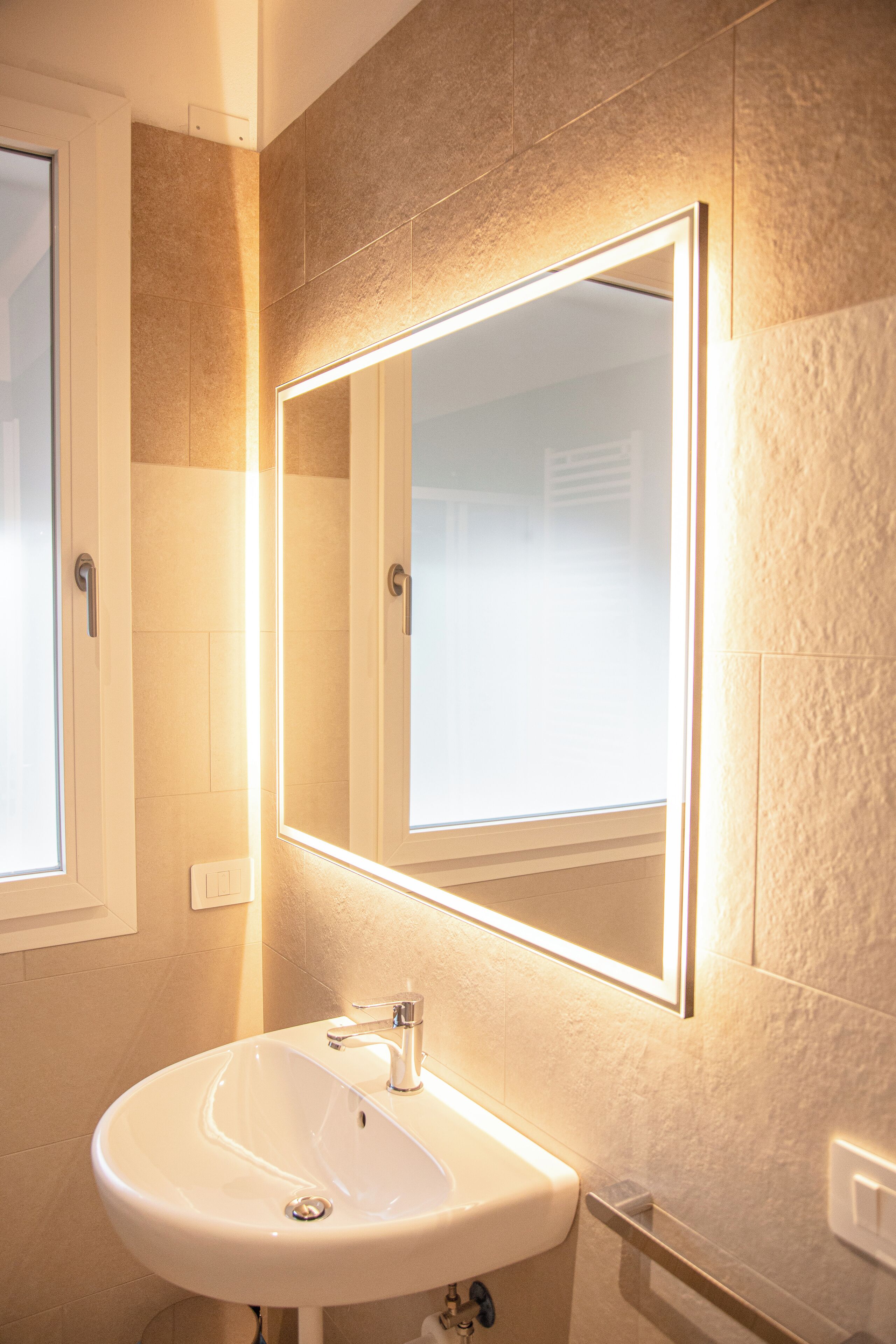A bathroom with a white sink, a mirror, and a lighted wall.