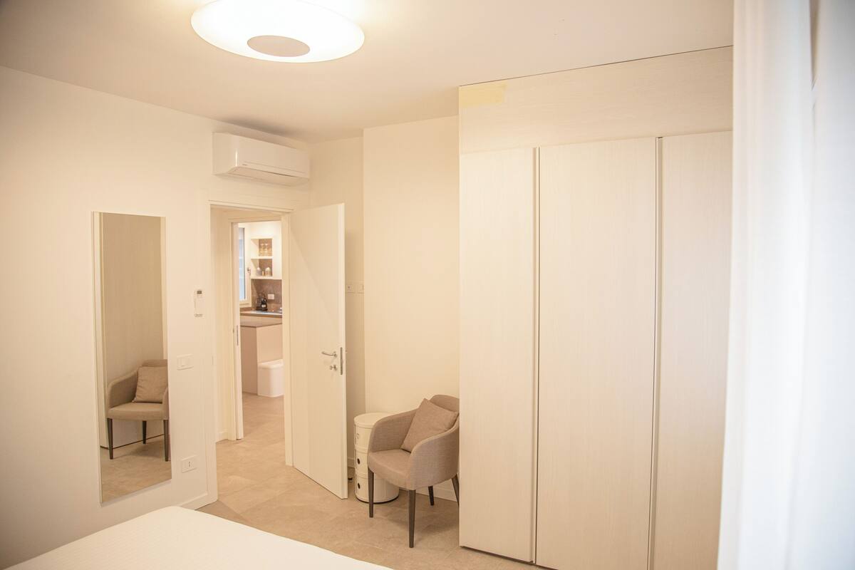 A hotel room with a bed, a wardrobe, a chair, and a bathroom visible through an open door.