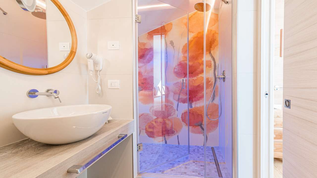 A bathroom with a large white sink, a mirror, a hairdryer, and a glass shower enclosure with a floral design.