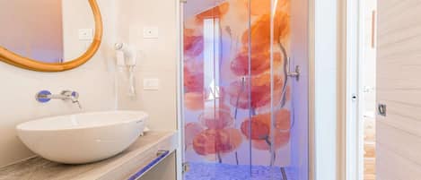 Un baño con un lavabo grande de color blanco, un espejo, un secador de pelo y un box de ducha de vidrio con un diseño floral.