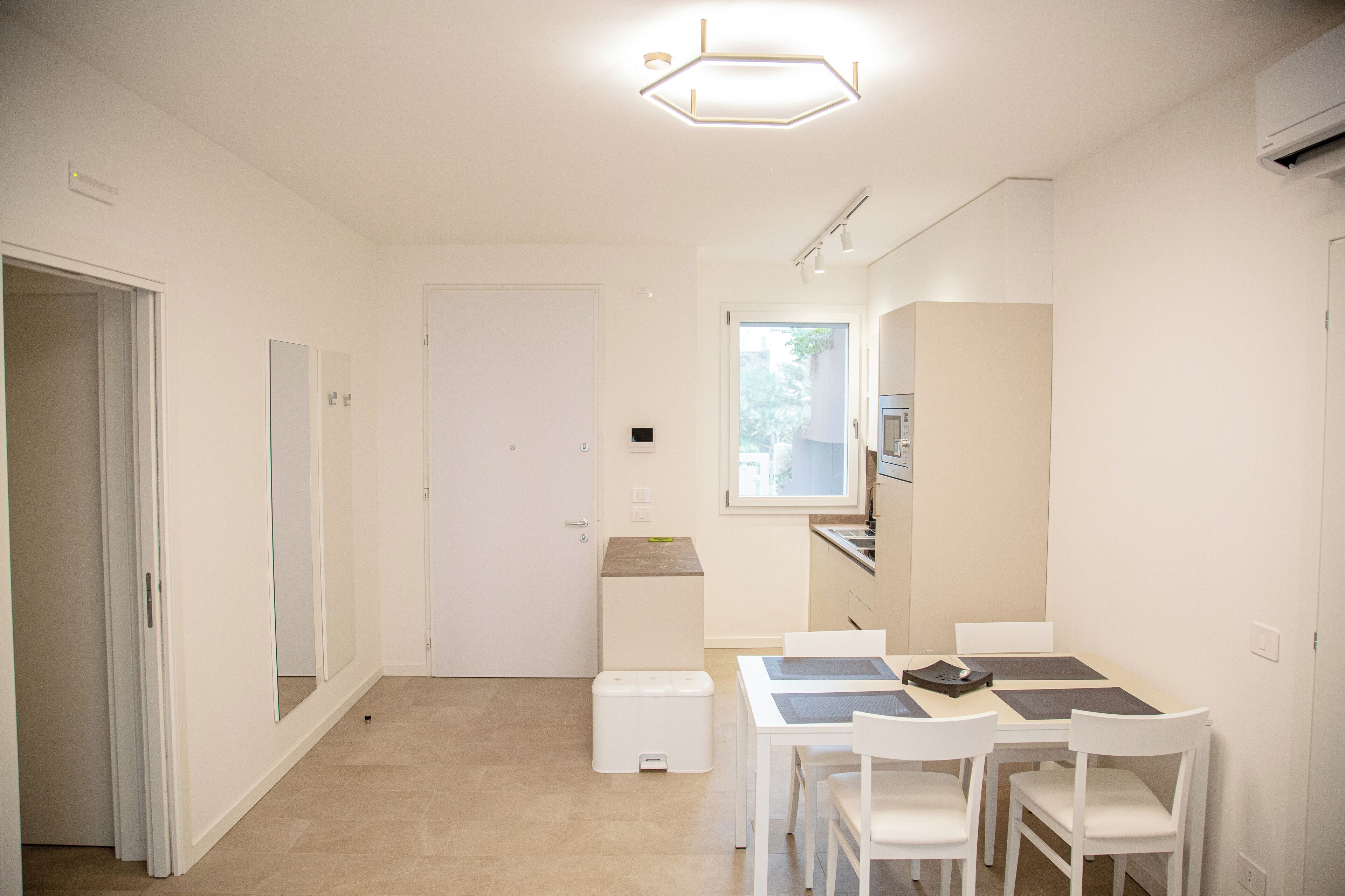 Een moderne, goed verlichte kamer met een eethoek, een kleine kitchenette en een deur naar een andere kamer.