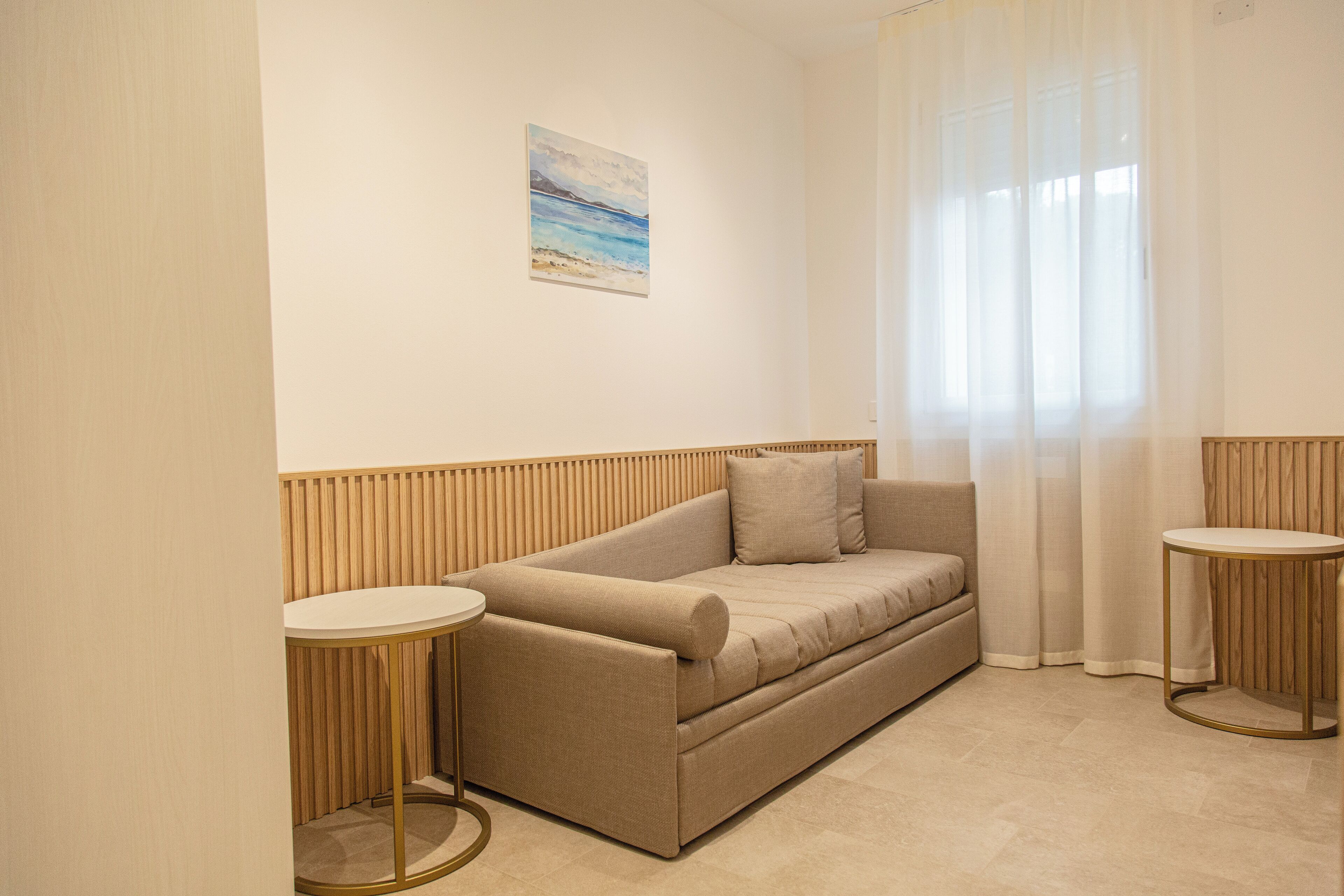 A modern, minimalist room with a beige sofa, two round tables, and a painting on the wall.
