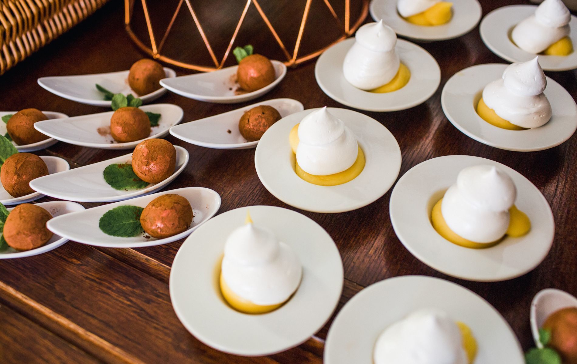 A table with plates of food, including white meringue-topped desserts and round, brown items, possibly cookies or pastries, on a wooden table.