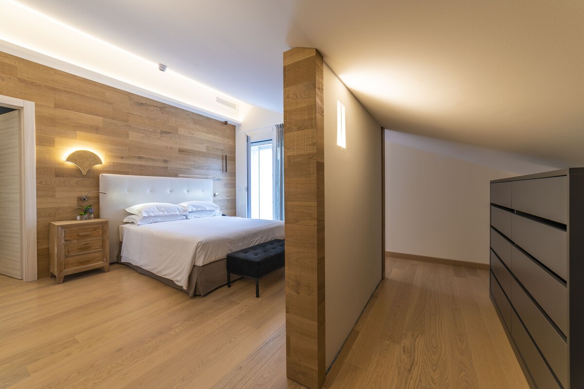 A bedroom with a wooden wall, a bed, a nightstand, and a dresser.