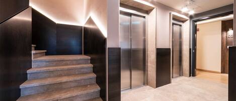 Un espace moderne abritant un ascenseur, avec un escalier menant à un étage supérieur.