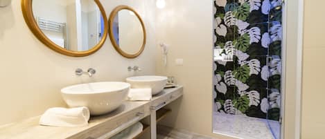 A modern bathroom with two sinks, a mirror, and a shower with a leaf-patterned wall.