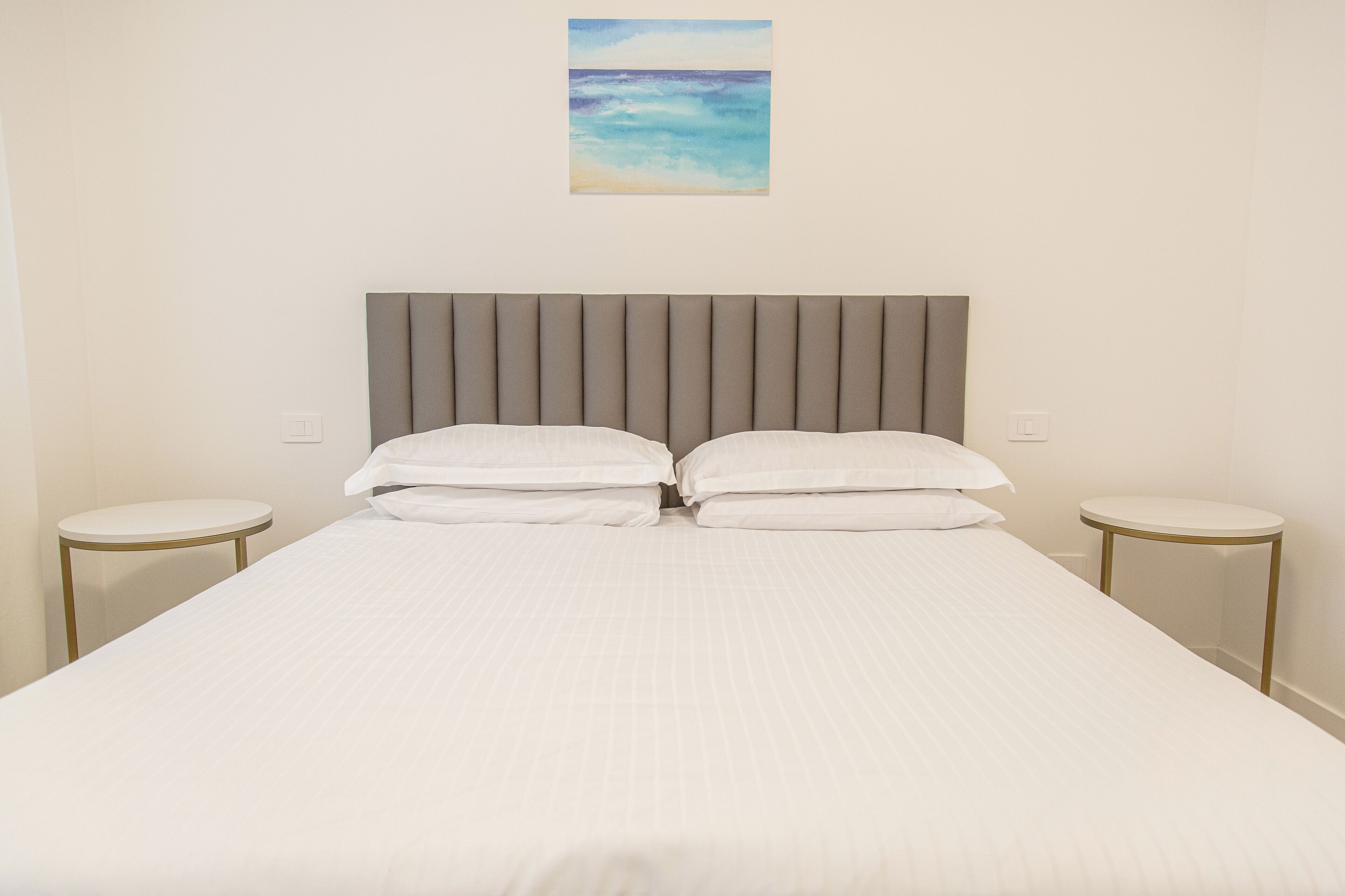A neatly made bed with a headboard, two bedside tables, and a painting on the wall.