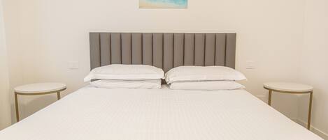 A neatly made bed with a headboard, two bedside tables, and a painting on the wall.