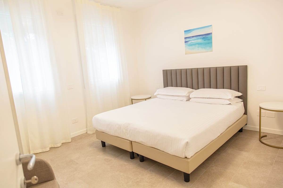 A neatly made bed with a grey headboard, two bedside tables, and a painting on the wall.