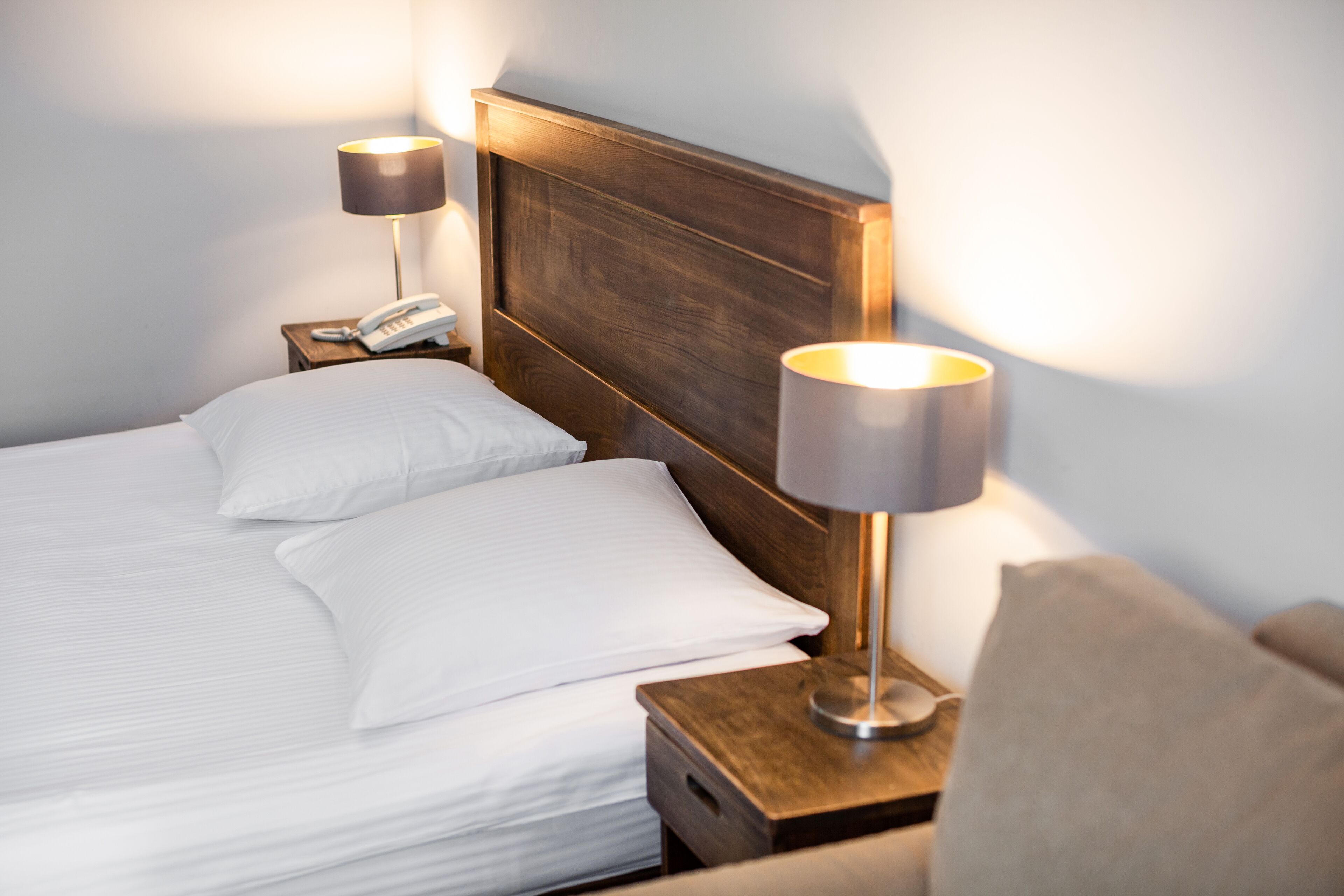 Ein ordentlich bezogenes Bett mit weißen Leinentüchern, einem Holz-Kopfbrett und zwei Nachttischlampen auf Holznachttischen.